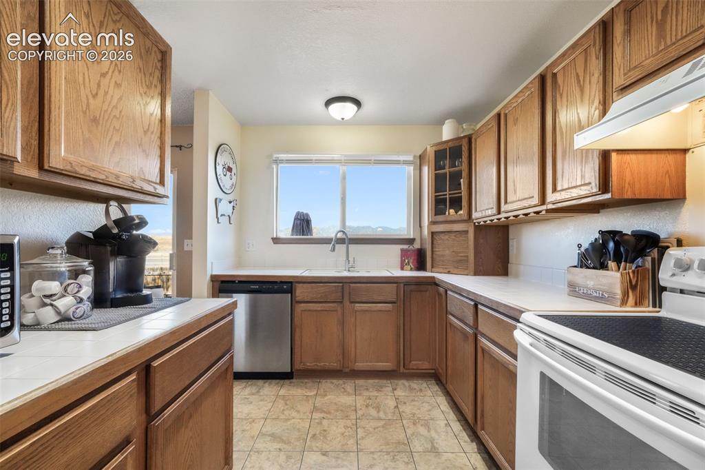 Image 16 of 50: Kitchen featuring wood cabinetry, white tile countertops, stainless steel d