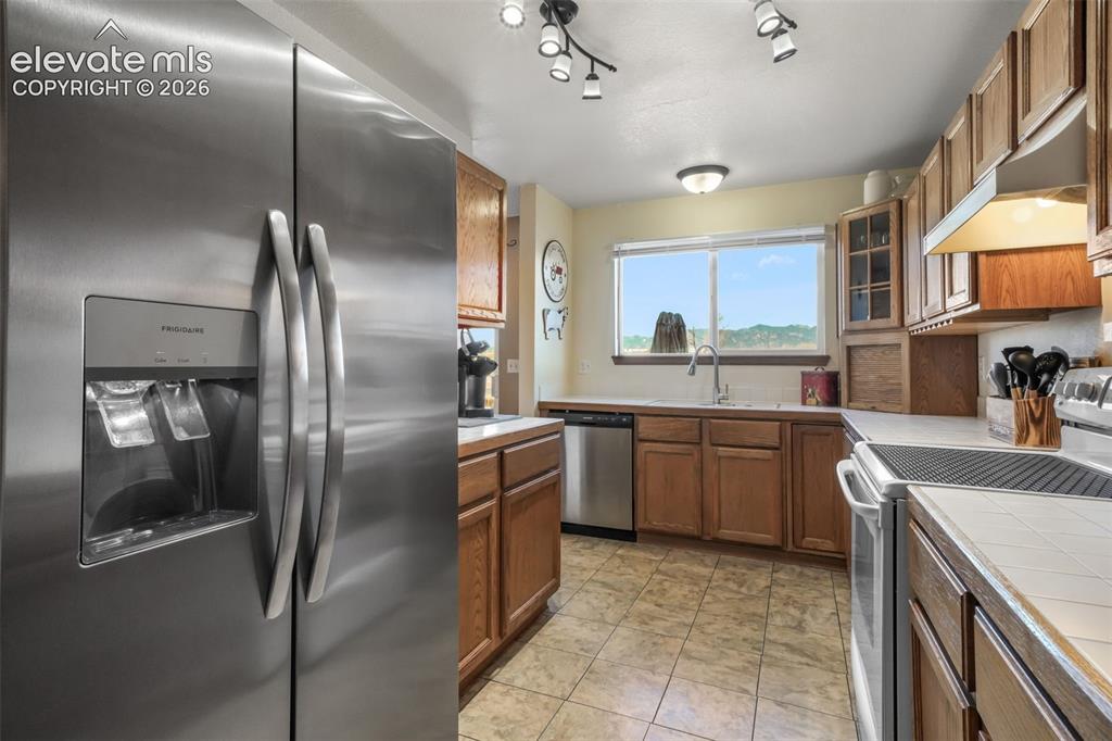 Image 17 of 50: Kitchen featuring stainless steel refrigerator, tile flooring, wood cabinet