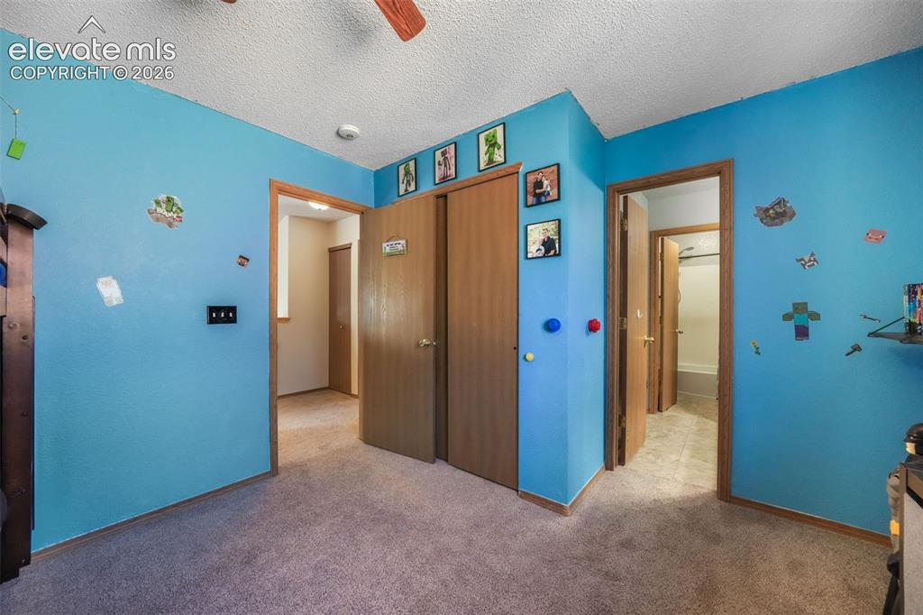 Image 26 of 50: Carpeted room with a ceiling fan, featuring multiple wood-finish doors and
