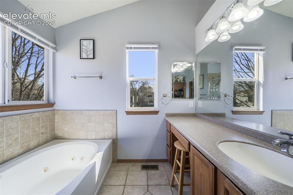 Image 33 of 50: Bathroom featuring a jetted soaking tub with tile surround, vaulted ceiling
