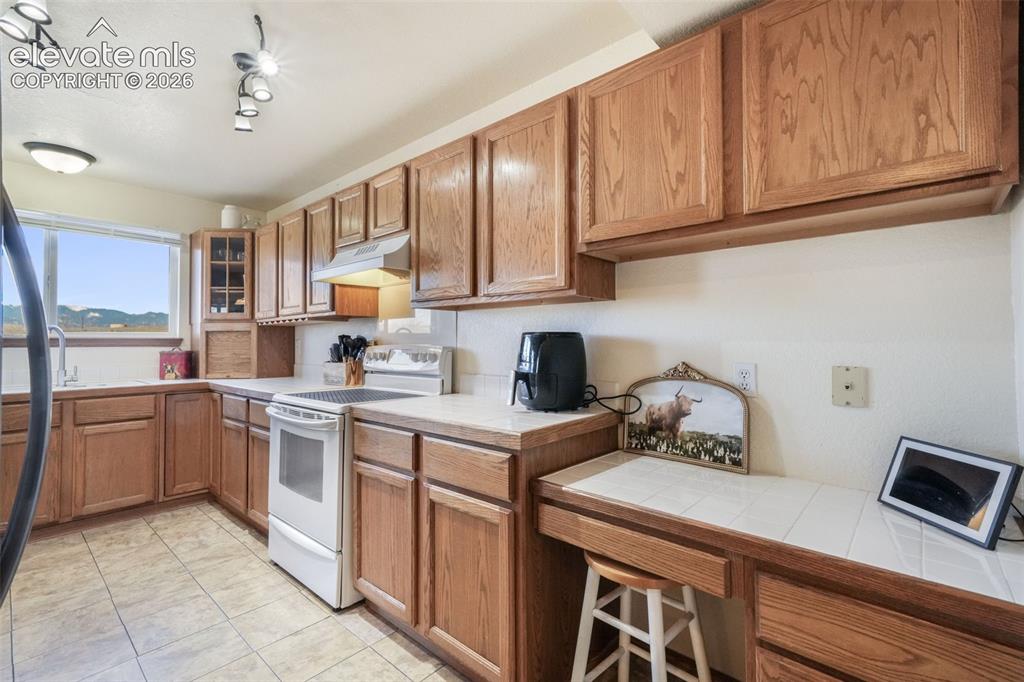 Image 38 of 50: Kitchen featuring wood cabinetry, light-toned countertops, a built-in desk